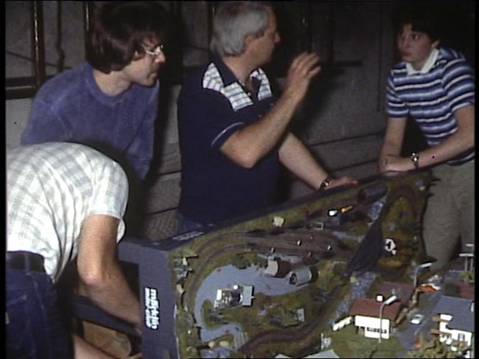 Mehrere Mitglieder des MEC Gernsheim besprechen die Arbeiten an der Modellbahnanlage, auf der bereits Gleise, Häuser und Landschaftsteile zu sehen sind.