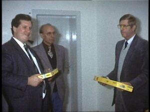 Drei Männer in Anzügen bei der offiziellen Übergabe der Clubräume des MEC Gernsheim am 10. Oktober 1985. Zwei von ihnen halten gelbe Gegenstände in den Händen.