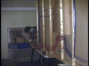 Blick auf die technische Verkabelung der Modellbahnanlage mit zahlreichen Kabeln und Leitungen entlang einer Holzkonstruktion. Im Hintergrund arbeitet ein Vereinsmitglied.