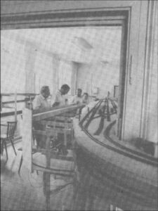 Historische Schwarz-Weiß-Aufnahme des MEC-Clubraums im Jahr 1988. Im Vordergrund verlaufen zahlreiche Gleistrassen der noch im Bau befindlichen Modellbahnanlage, im Hintergrund sind mehrere Personen zu sehen.