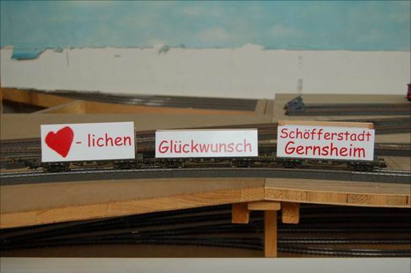 Drei Modellbahnwagen mit den Aufschriften „Herzlichen Glückwunsch Schöfferstadt Gernsheim“ stehen auf der noch im Bau befindlichen Vereinsanlage des MEC. Der Zug gratuliert der Stadt zum 850-jährigen Jubiläum im Jahr 2006.