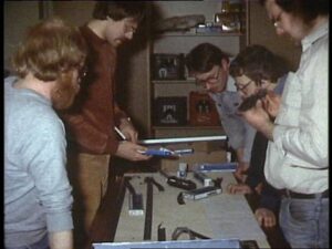 Mehrere Vereinsmitglieder stehen um eine Tischfläche mit Gleismaterial und besprechen 1984 gemeinsam die geplante Streckenführung der Modellbahnanlage.