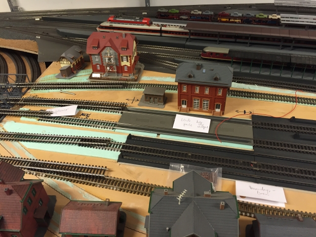 Stellprobe für das geplante Bahnbetriebswerk mit mehreren Modellgebäuden und noch nicht fertig verlegten Gleisen neben dem provisorischen Bahnhof.