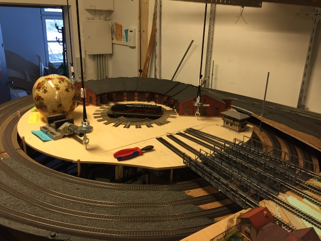 Baustelle des Bahnbetriebswerks mit Drehscheibe, halbkreisförmigem Ringlokschuppen, mehreren Zufahrtsgleisen und einer Lokomotive auf der Drehscheibe.