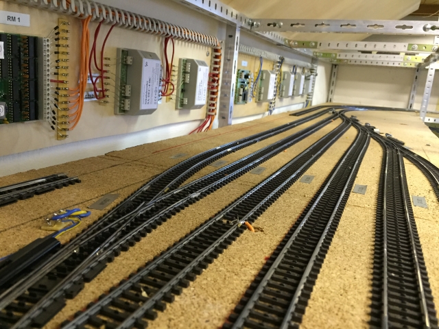 Mehrere Gleise und Weichen des Schattenbahnhofs 3xx auf einer Korkunterlage, daneben an der Wand montierte Elektronikmodule mit Verkabelung.