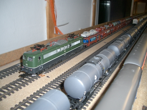 Grüne Elektrolokomotive neben einem Zug mit silbernen Wagen und weiteren abgestellten Modellzügen
