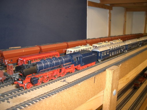 Blaue Dampflokomotive mit roten Rädern vor historischen Doppelstockwagen auf der Modellbahnanlage