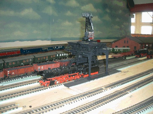Historische Aufnahme des Bahnbetriebswerks der Modellbahnanlage mit einer schwarzen Dampflokomotive vor einem großen Bekohlungskran. Im Hintergrund stehen weitere Lokomotiven, Personenwagen und rote Betriebsgebäude.