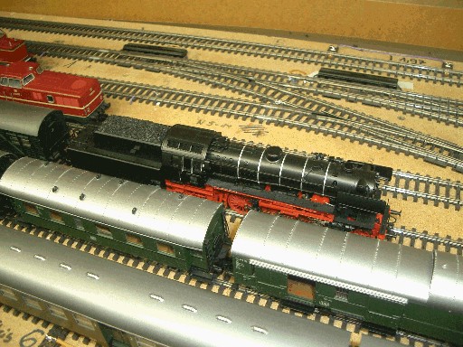 Schwarze Dampflokomotive der Baureihe 23 mit rotem Fahrwerk zwischen abgestellten Reisezugwagen auf der Modellbahnanlage