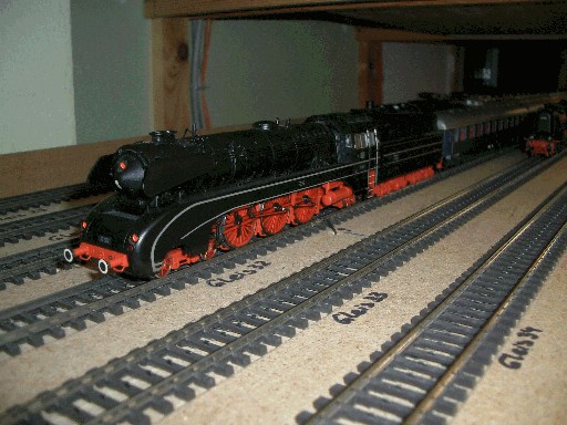 Schwarze Märklin-Dampflokomotive der Baureihe 10 mit roten Rädern und angehängten Reisezugwagen auf einem Abstellgleis