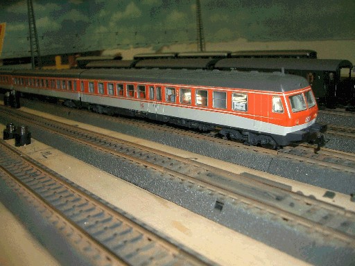 Rot-weißer Modelltriebwagen der Baureihe 614 mit beleuchtetem Innenraum auf einem Gleis der Modellbahnanlage