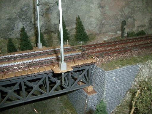 Ende einer zweigleisigen Modellbahn-Fachwerkbrücke mit Geländer, Oberleitungsmast und gemauertem Brückenwiderlager