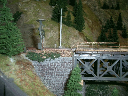 Linkes Ende einer grauen Modellbahn-Fachwerkbrücke mit feinem Geländer, Vorsignal und bewachsenem Bahndamm