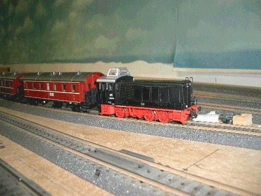 Schwarze Lenz V36 mit roten Anhängern auf einem Gleis.