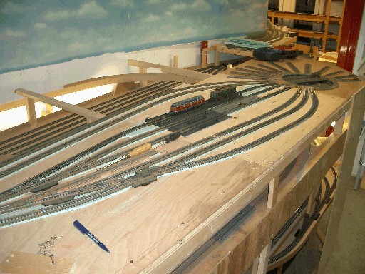 Bahnbetriebswerk im Bau mit mehreren Gleisen, Weichen und zwei abgestellten Modelllokomotiven auf einer noch ungestalteten Holzplatte.