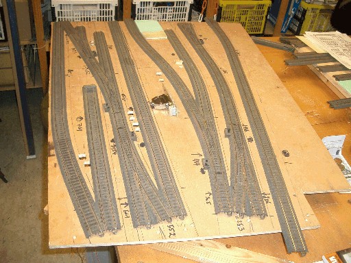 Holzplatte mit ausgelegten Modellbahngleisen und Weichen für ein weiteres Bahnhofsmodul im Bau.