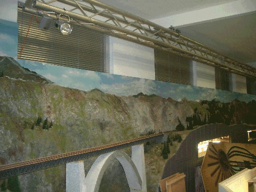 Geschlossene Jalousien an den hohen Fenstern oberhalb der Modellbahnanlage. Darunter verläuft die Paradestrecke entlang einer felsigen Gebirgslandschaft mit Brücke.