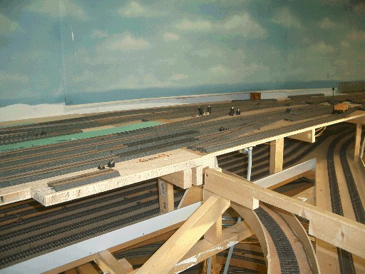 Mehrstöckiger Rohbau der Modellbahnanlage mit zahlreichen Gleisen auf mehreren Ebenen. Oben liegt der Hauptbahnhof, darunter verlaufen Gleise der Schattenbahnhöfe und geschwungene Fahrtrassen auf einer offenen Holzkonstruktion.