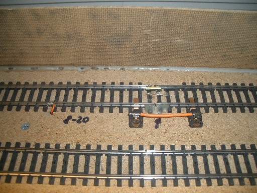 Modellbahngleis mit aufgetrennter Schiene, orangefarbener Kabelverbindung und alter Klebestelle