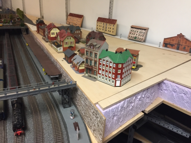 Erste Stellprobe für Schöfferstadt: Mehrere Modellhäuser stehen lose auf einer noch ungestalteten Holzfläche oberhalb der Bahnsteige.