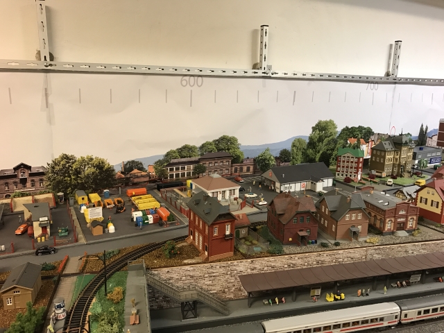 Blick auf den rechten Teil der Modellstadt Schöfferstadt mit Wohnhäusern, Gewerbegebäuden und Straßen oberhalb des Bahnhofs. Dahinter ist die teilweise gestaltete Hintergrundkulisse zu sehen.