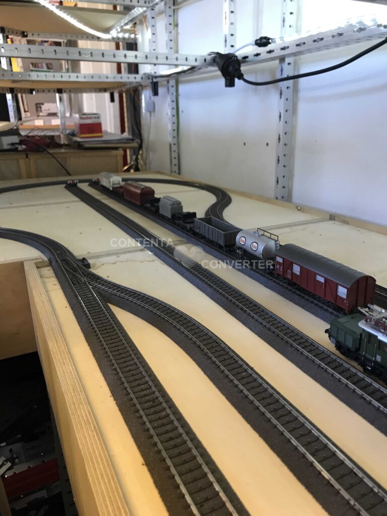 Historische Aufnahme der MEC-Testanlage mit mehreren Gleisen, Weichen und abgestellten Güterwagen auf einer einfachen Holzplatte unterhalb der großen Modellbahnanlage.