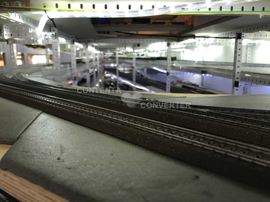 Nahaufnahme mehrerer parallel verlaufender und gebogener Modellbahngleise auf einer beleuchteten Ebene unter der Schöfferstadt.