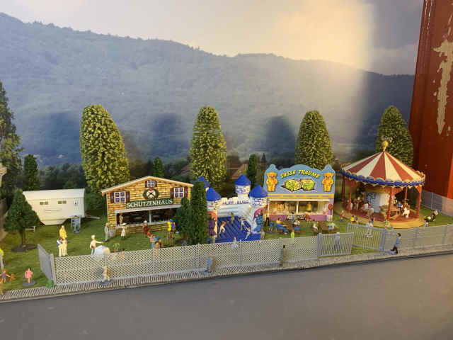Kirmes auf der Modellbahnanlage des MEC Gernsheim mit Kinderkarussell, Süßigkeitenstand, Hüpfburg und Schützenhaus. Zahlreiche kleine Figuren beleben das eingezäunte Festgelände.