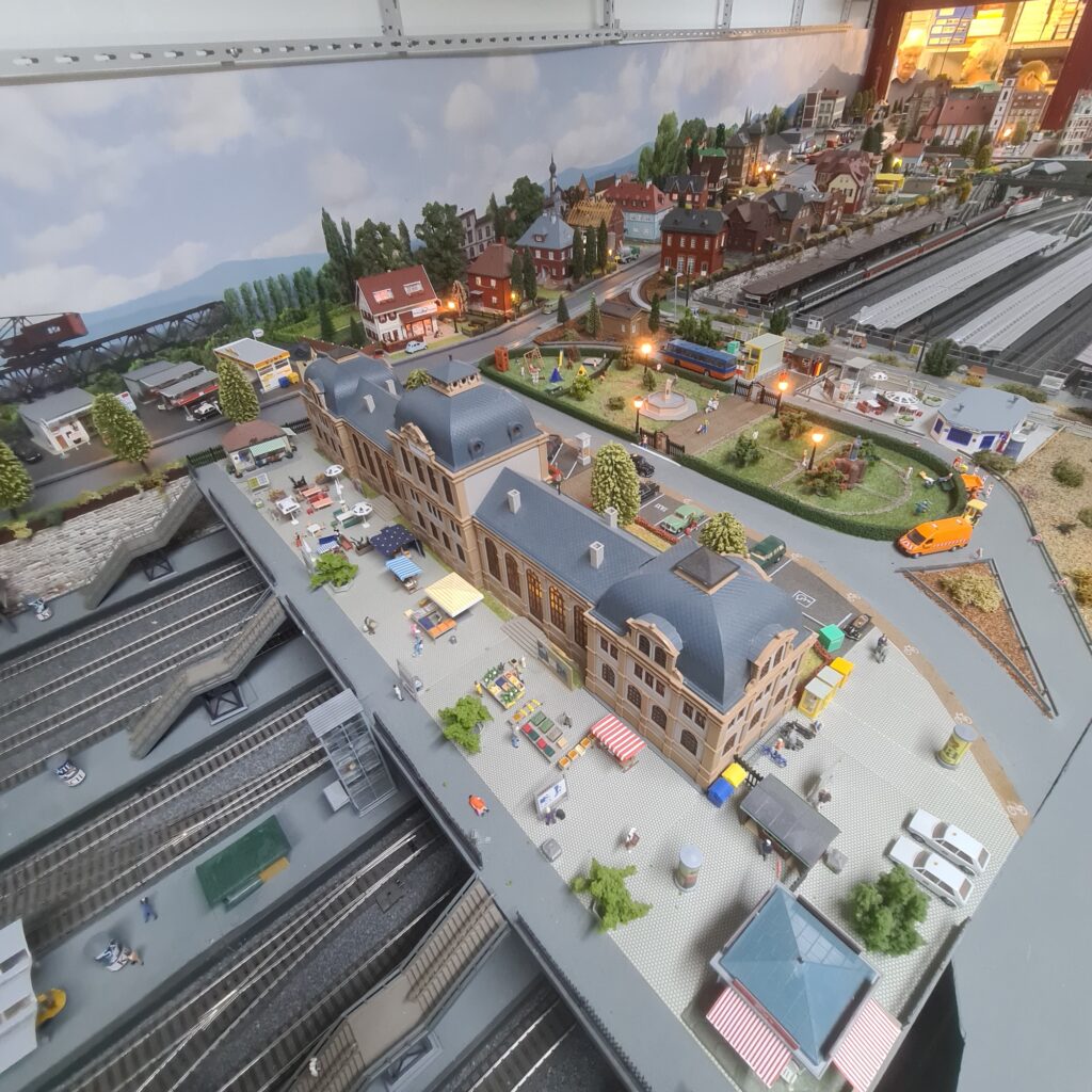 Gesamtansicht des Modellbahnhofs mit Bahnsteigen, Vorplatz und angrenzender Stadt.