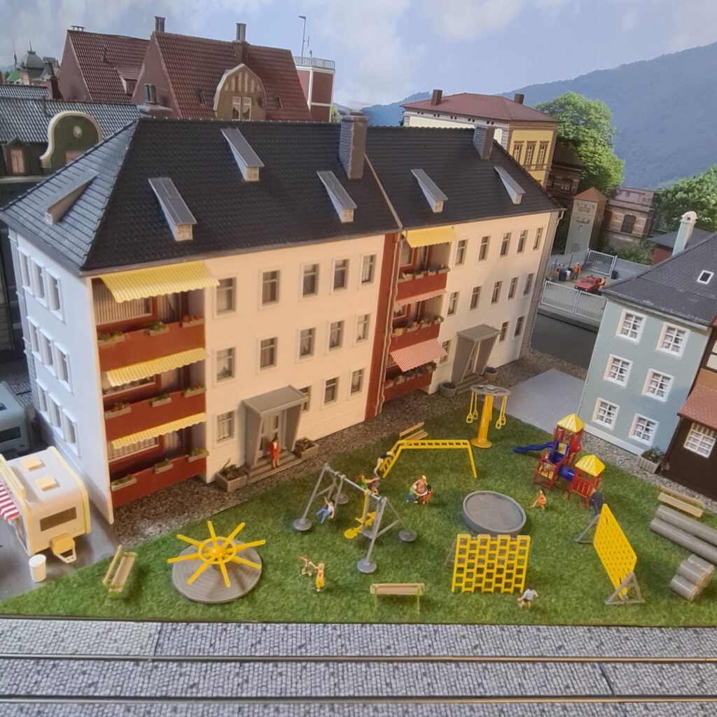 Spielplatz mit Schaukeln, Klettergeräten und Spielfiguren im Innenhof mehrerer Wohnhäuser.