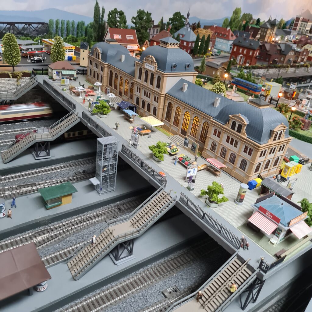 Modellbahnhof Schöfferstadt Hbf mit großem Empfangsgebäude, Bahnhofsvorplatz und mehreren Bahnsteigen.