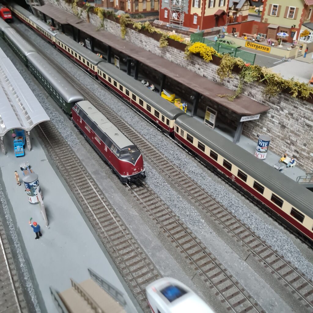 Rot-beige Triebwagen und Personenzüge an den Bahnsteigen des Modellbahnhofs.