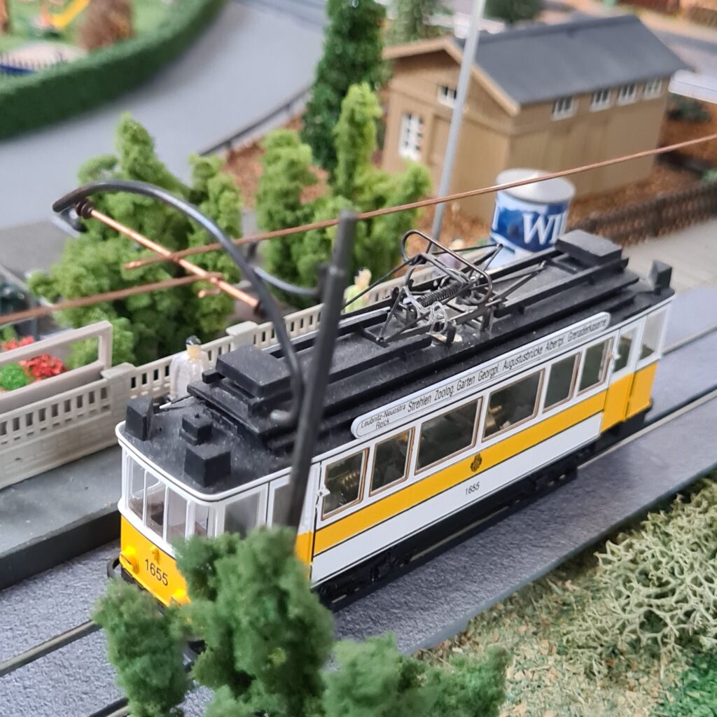 Gelb-weiße historische Straßenbahn mit der Wagennummer 1655 unter einer Oberleitung auf der Modellbahnanlage.