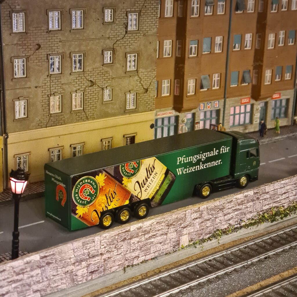 Grüner Lastwagen mit Werbeaufschrift fährt an mehrstöckigen Stadthäusern entlang.