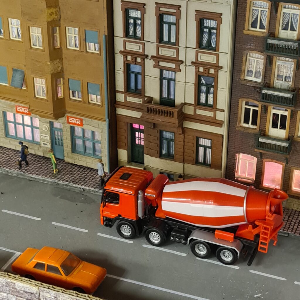 Roter Betonmischer und Pkw auf einer Straße vor mehrstöckigen Wohnhäusern.