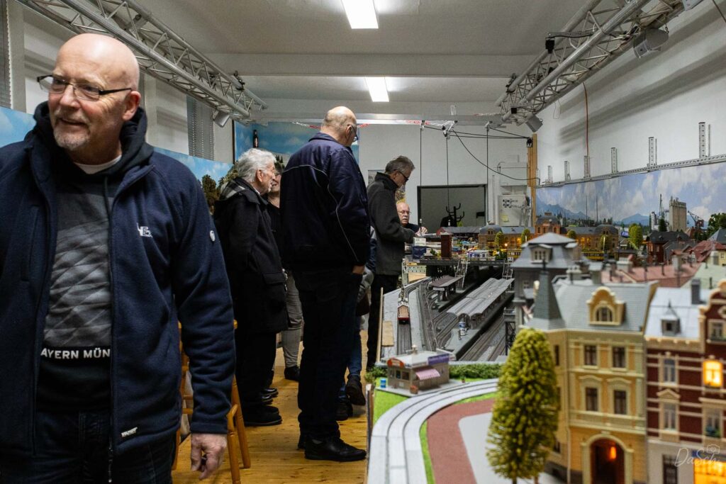 Mehrere Besucher betrachten beim Publikumsfahrtag die Modellbahnanlage des MEC Gernsheim mit ihren Gleisen, Gebäuden und Landschaften.