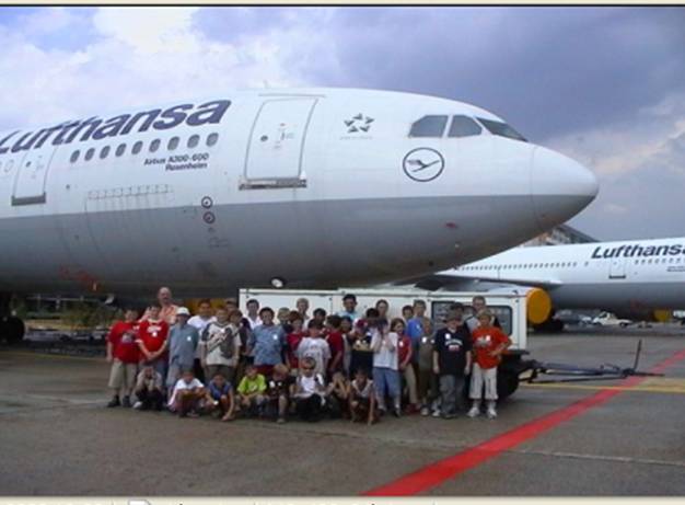 Kinder und Betreuer bei einem Ausflug zum Flughafen vor einem Lufthansa-Flugzeug.