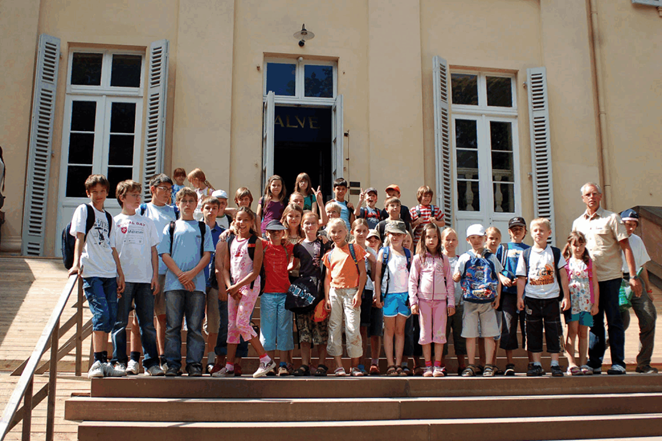Gruppe von Kindern und Betreuern auf einer Treppe vor einem großen Gebäude.