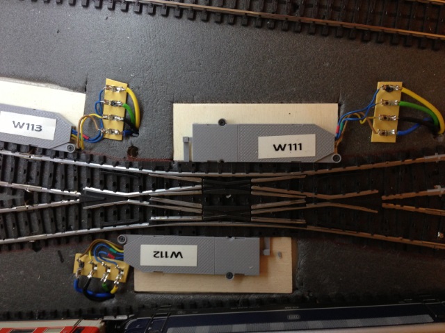 Nahaufnahme einer Modellbahnweiche mit zwei beschrifteten Weichenantrieben W111 und W112