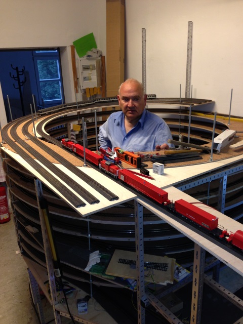 Volker sitzt im Gleiswendel der Vereinsanlage. Vor ihm steht ein roter Tunnelrettungszug auf der provisorischen Teststrecke.