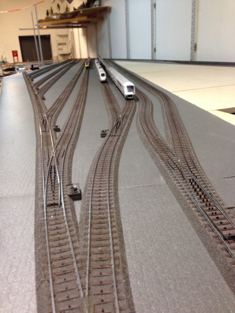 Mehrgleisiger Bahnhof im Rohbau mit Weichen und mehreren abgestellten Modellbahnzügen