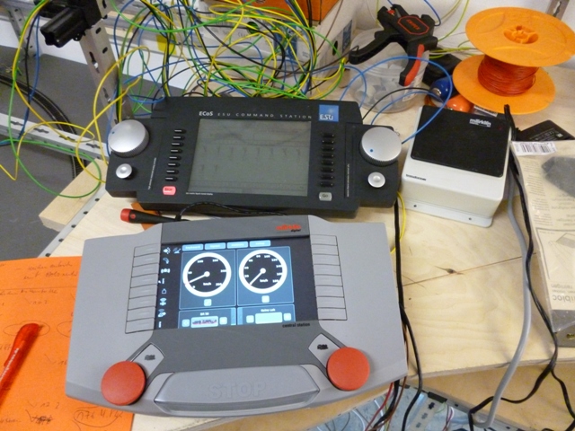 Zwei digitale Modellbahn-Steuergeräte mit Displays auf einem Arbeitstisch, umgeben von Kabeln