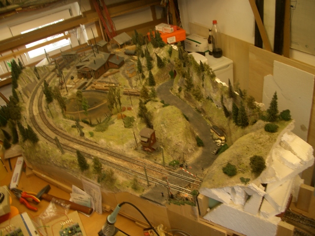 Modellbahn-Landschaftsmodul mit bewaldeten Hügeln, Straßen, Gebäuden und Eisenbahngleisen