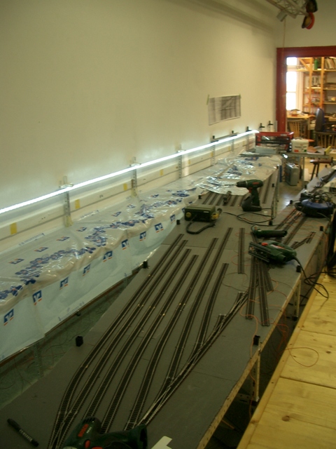 Unterste Ebene des Schattenbahnhofs im Aufbau mit bereits verlegten K-Gleisen, Werkzeugen und eingeschalteter Lichtleiste entlang der Wand.