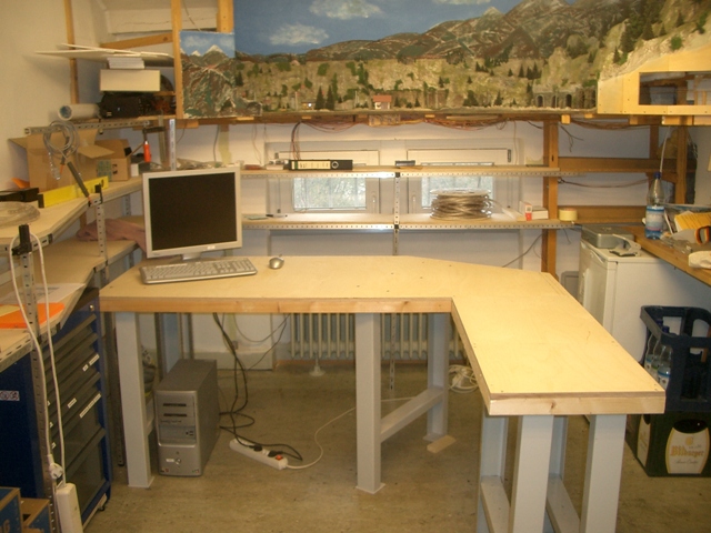 U-förmiger Arbeitsplatz mit Computer unter einer Modellbahn-Landschaftskulisse