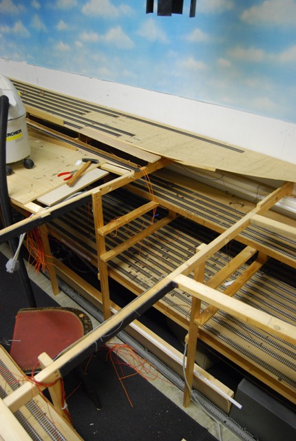 Blick auf die zurückgebaute Modellbahnanlage mit verbliebenen Gleisen, offenen Holzrahmen und Himmelskulisse.