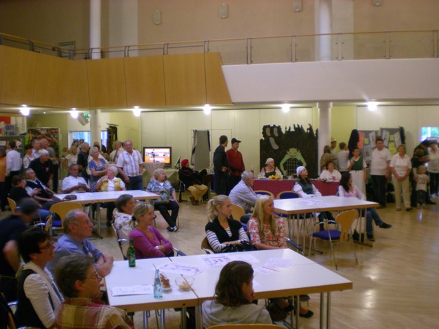 Besucherinnen und Besucher sitzen und stehen an Tischen in einem Veranstaltungssaal.