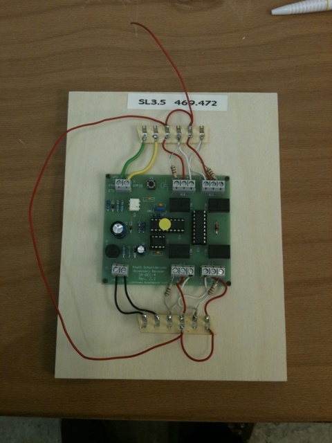 Elektronische Steuerplatine auf einer Holzplatte mit angeschlossenen Kabeln und Anschlussklemmen